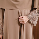Close-up of a person wearing a beige abaya with intricate lace detailing on the sleeves by Tubita.