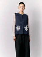 Woman wearing a navy vest with white floral embroidery by Studio Tui on a plain background