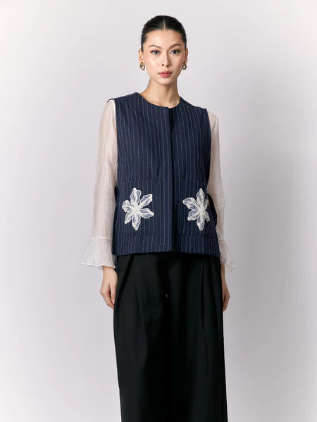 Woman wearing a navy vest with white floral embroidery by Studio Tui on a plain background