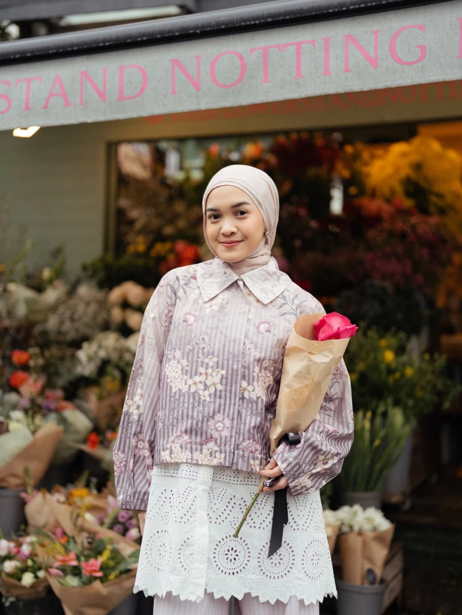 Woman wearing floral jacket by Haidee Orlin holding a bouquet of flowers in front of a floral stand with 'Notting' visible