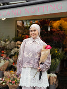 Woman wearing floral jacket by Haidee Orlin holding a bouquet of flowers in front of a floral stand with 'Notting' visible