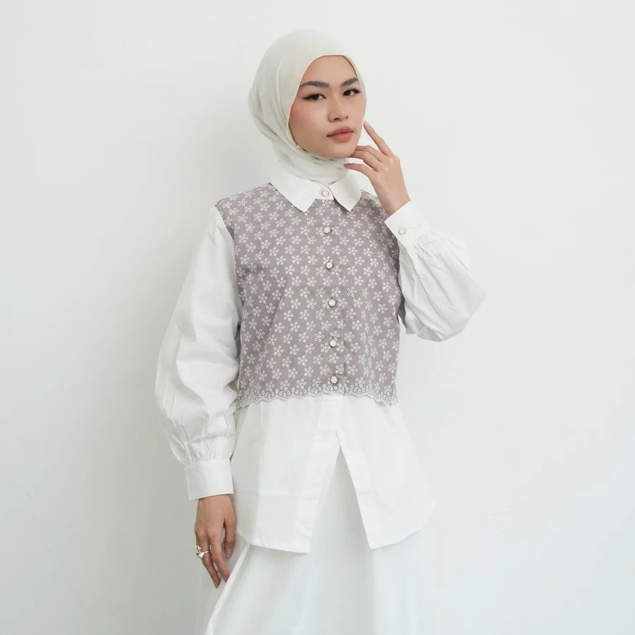 Woman wearing a white blouse by Tunique with a patterned vest-like details against a plain background