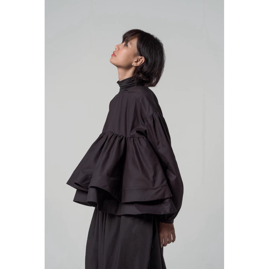 Person wearing a black layered blouse by Yestoday and skirt set against a plain background