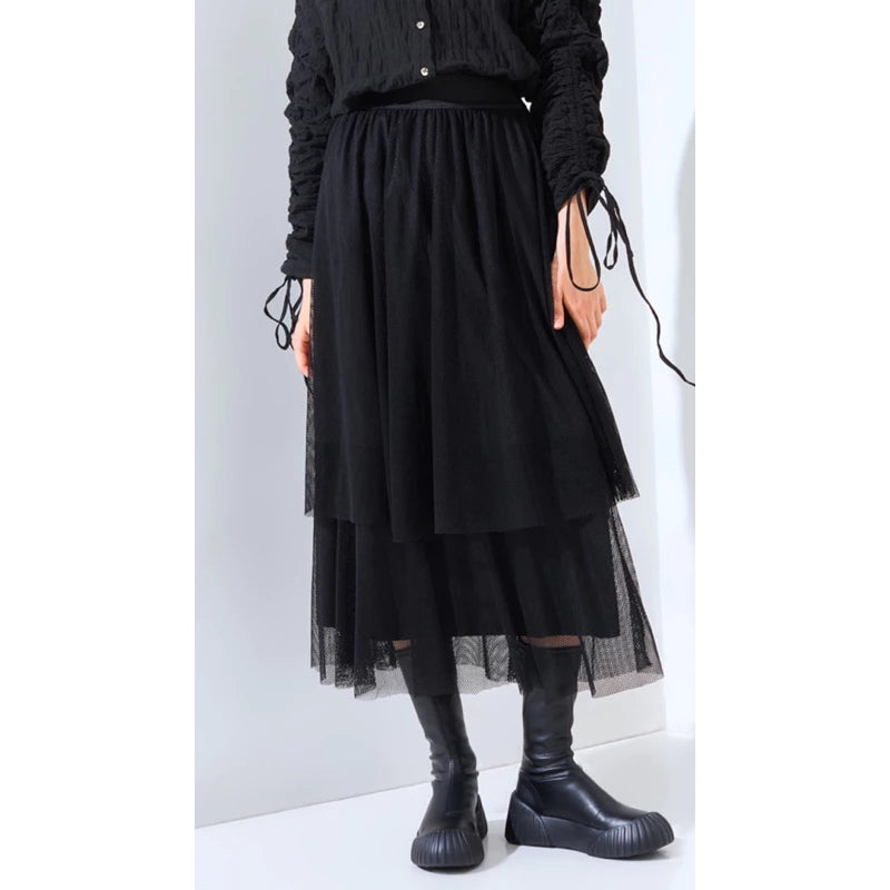 A person wearing a layered black skirt by Yestoday with a elastic waistband and black boots. The skirt has a solid color and appears to be made of a smooth fabric with a flared design.
