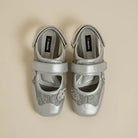 Pair of silver flat shoes with decorative elements by Dianable on a beige background