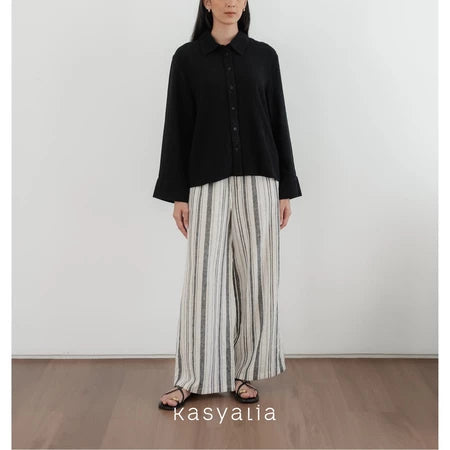Person wearing a black shirt and striped pants standing against a white wall with 'kasyalia' branding.