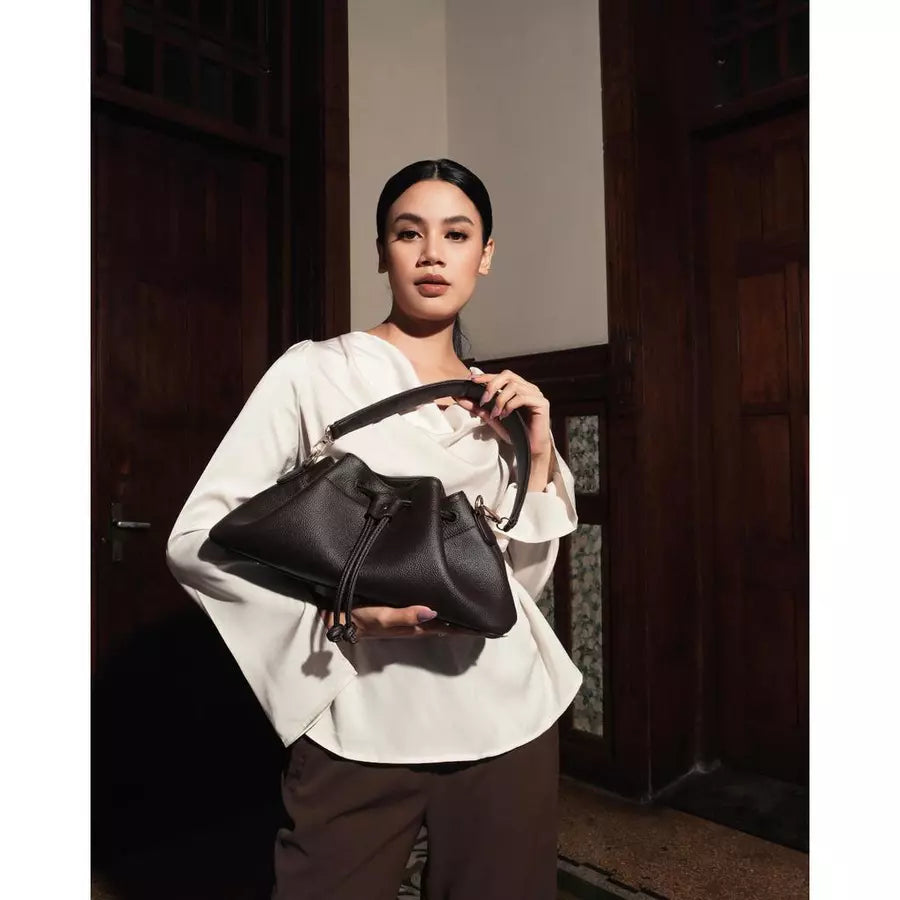 Woman holding a dark brown shoulder bag by Prior in a dimly lit room