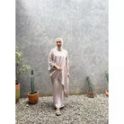 Woman in a light-colored outfit set by Abame standing in front of a textured wall with potted plants.