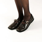 Brown flat shoes by Cekhas with buckles worn by a person on a white background