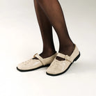 Beige leather falt shoes by Cekhas with black soles worn with black tights on a white background