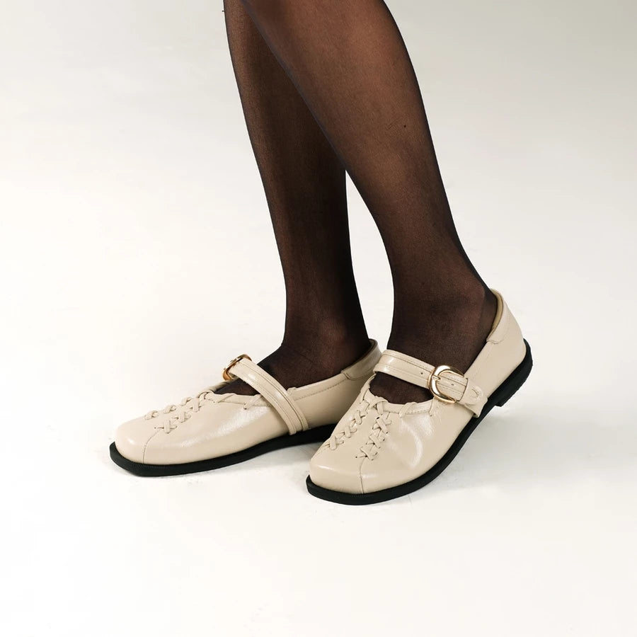 Beige leather falt shoes by Cekhas with black soles worn with black tights on a white background