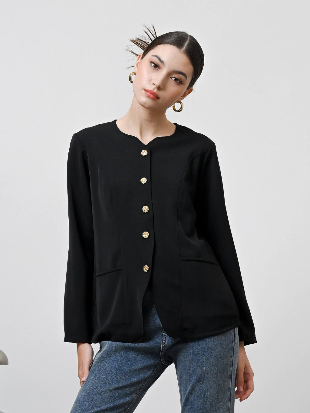 A woman wearing a black long-sleeved blouse with gold front buttons by Kasa Heritage, paired with blue jeans.