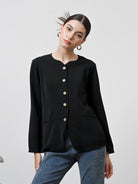 A woman wearing a black long-sleeved blouse with gold front buttons by Kasa Heritage, paired with blue jeans.