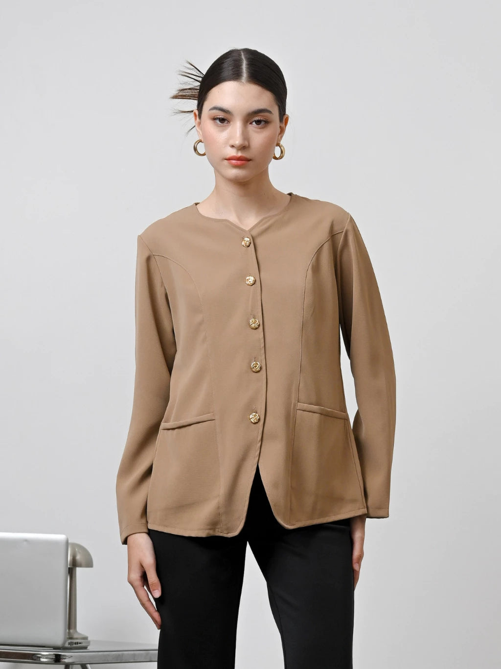 A woman wearing a brown long-sleeved blouse with gold front buttons by Kasa Heritage, paired with blue jeans.