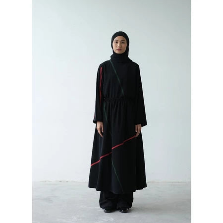 A person wearing a black Rashawl Levy pleated patch blouse with a hood, featuring a simple design with possibly pleats on the left hand.