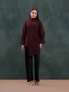 Woman wearing a burgundy blouse by Kasa Heritage and black pants against a dark green background