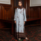 Woman wearing a light blue dress with brown-colored floral embroidery by Lozy Hijab in a room with wooden paneling.