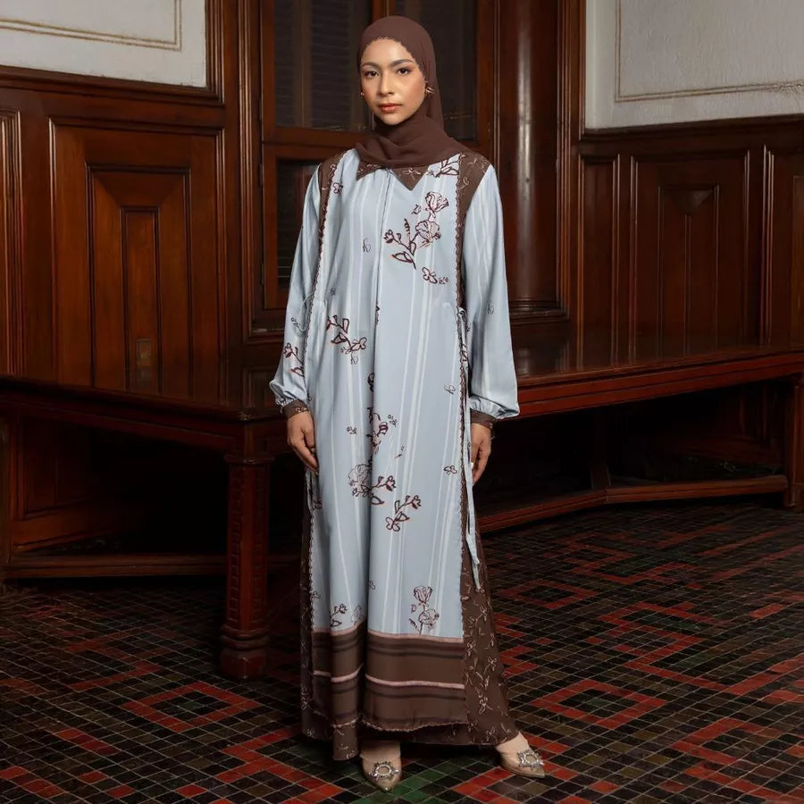 Woman wearing a light blue dress with brown-colored floral embroidery by Lozy Hijab in a room with wooden paneling.