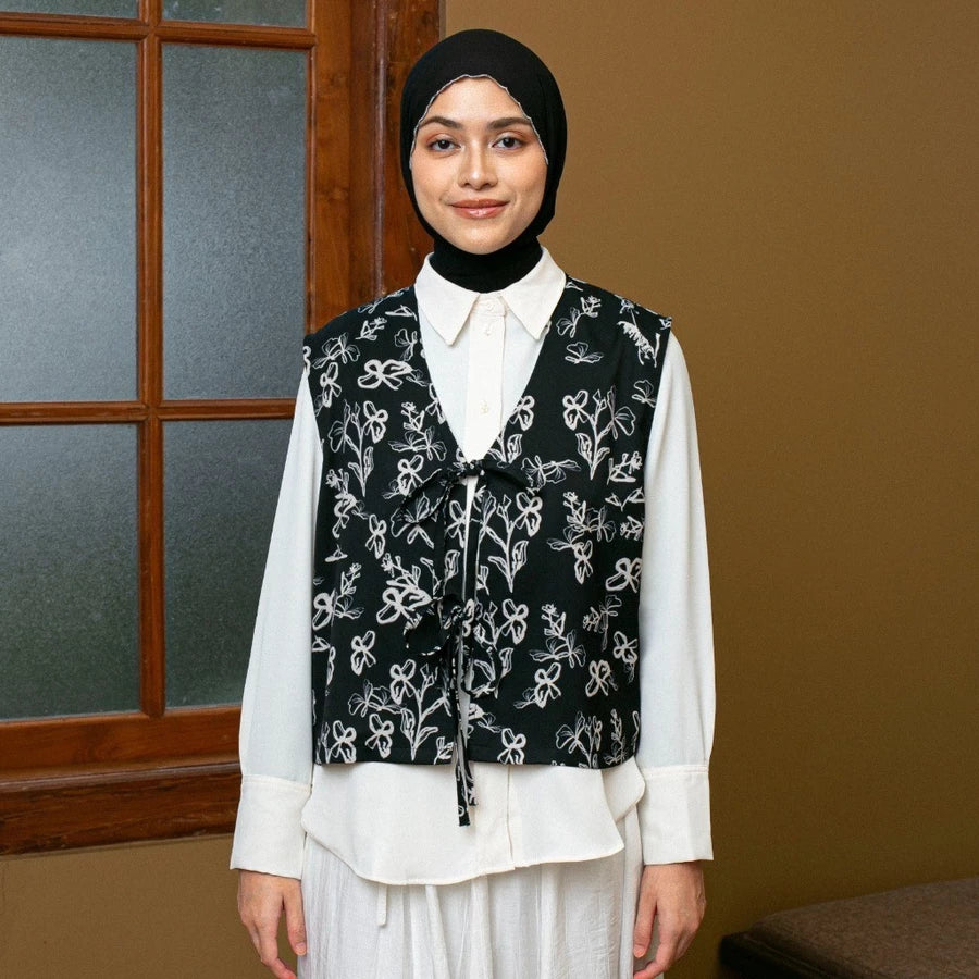 Woman wearing a black floral vest by Lozy Hijab over a white shirt in front of a window.