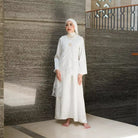 Woman in a white dress by Tunique standing against a textured wall.