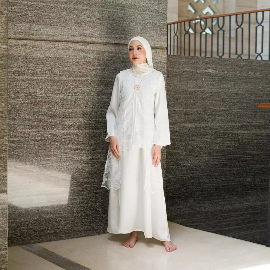 Woman in a white dress by Tunique standing against a textured wall.