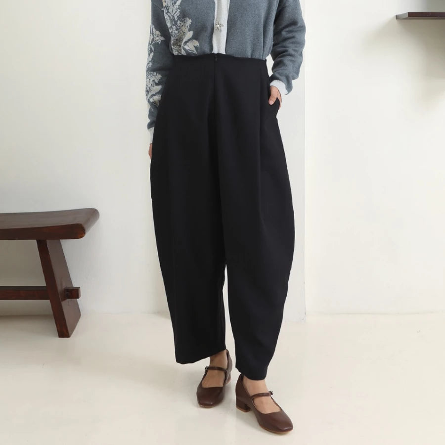 Person wearing black wide-leg pants by Hijabchic with a light gray cardigan and brown shoes in a minimalistic setting.