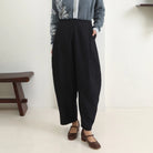 Person wearing black wide-leg pants by Hijabchic with a light gray cardigan and brown shoes in a minimalistic setting.