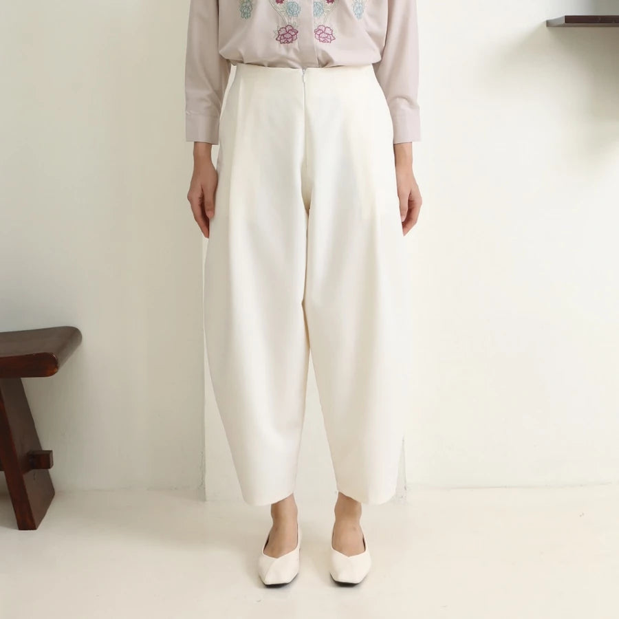 Person wearing white wide-leg pants by Hijabchic and a light-colored top with floral embroidery on a plain background