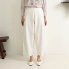 Person wearing white wide-leg pants by Hijabchic and a light-colored top with floral embroidery on a plain background