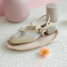 Beige mules sandal with decorative bow and flower by Dianable on a white surface with pink and gray background