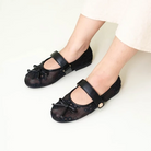 A pair of women's flat shoes by Dianable with lace detailing and small bows on the top, color black, worn by a person standing.