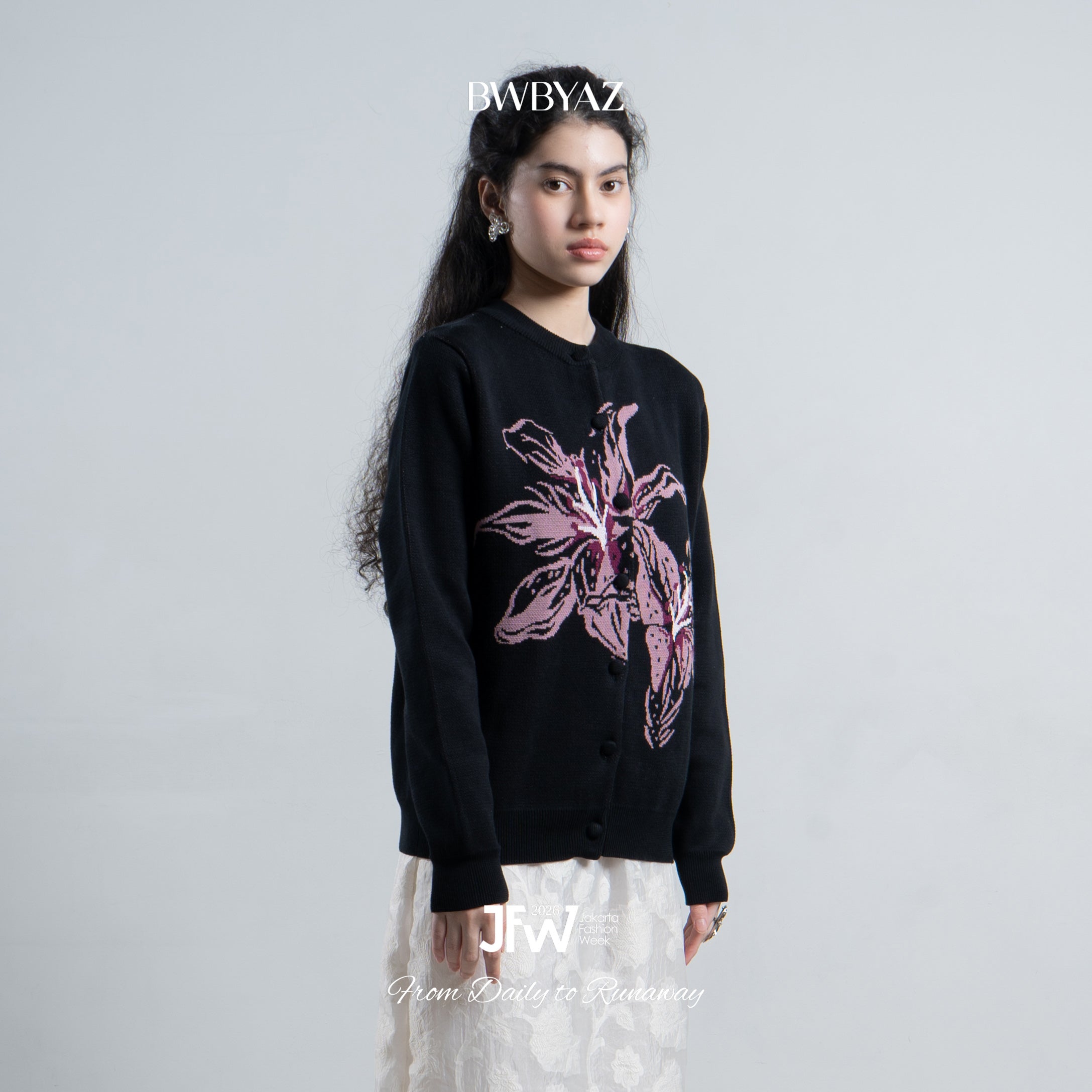Person wearing a black cardigan with pink floral design on a gray background, featuring the brand 'BWBYAZ'.