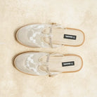 Pair of beige mules flat shoes with floral patterns on a beige background