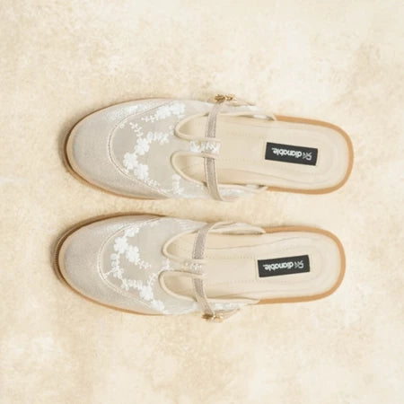 Pair of beige mules flat shoes with floral patterns on a beige background