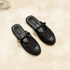 Black mules flat shoes with decorative straps by Dianable on a beige surface
