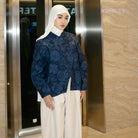 Woman in a navy blue patterned top by Haidee Orlin and white hijab standing in an elevator.