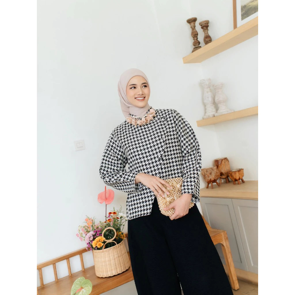 Woman wearing a checkered blouse from Haidee Orlin and hijab in a room with decor elements.