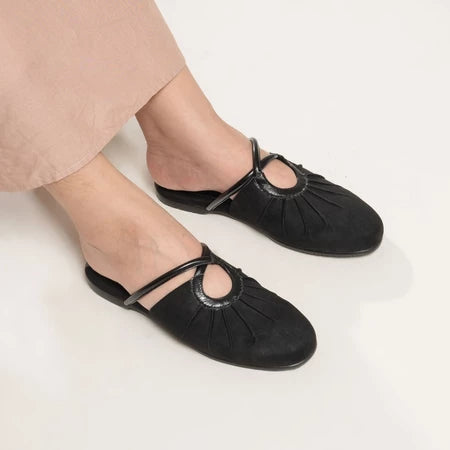 Black flat shoes from Dianable worn with beige pants on a light background