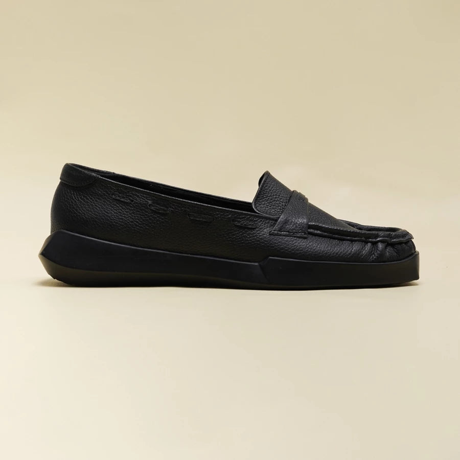 A single black leather slip-on loafer flatshoes by Cekhas with a textured pebbled upper and a chunky black platform sole, shown in profile against a solid beige background.