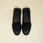 A pair of black leather penny loafers flatshoes with a chunky black sole, photographed from a top-down view on a light beige background. The brand name 'Cekhas' is visible on the insole.