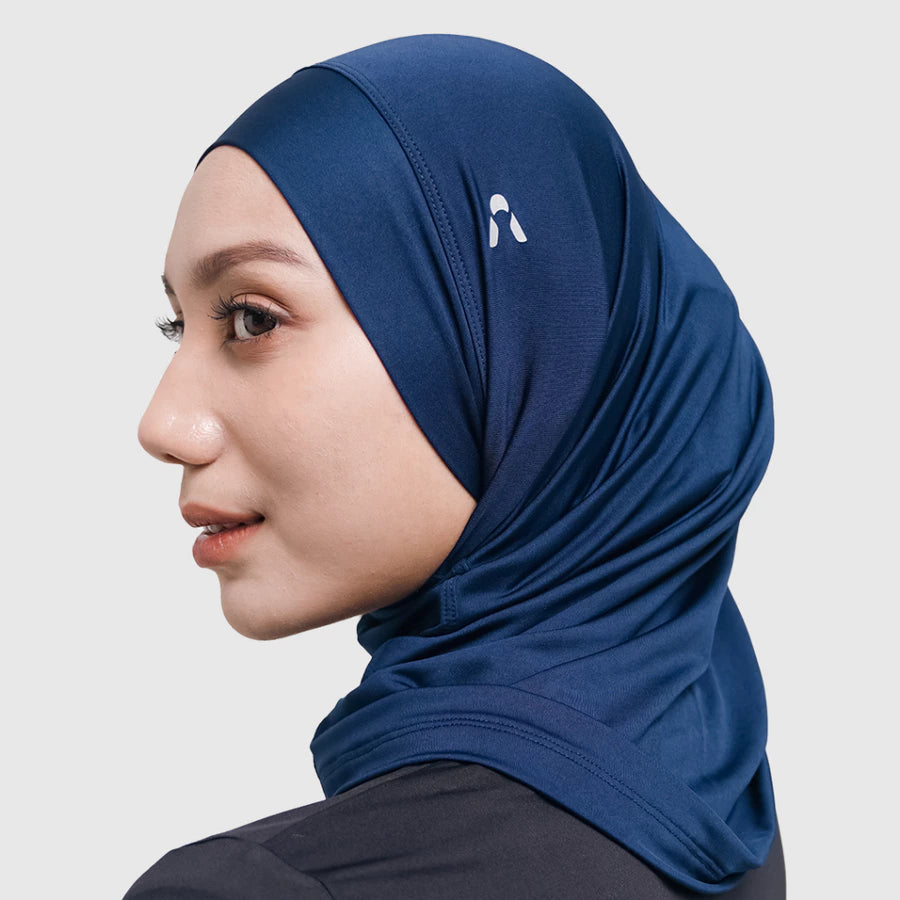 Woman wearing a navy sport hijab with a logo by HIA on a light gray background