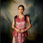 A woman wearing a sleeveless, flared, mauve colored top by Kartinis Label with velvet material and decorative elements on the shoulders and waist.