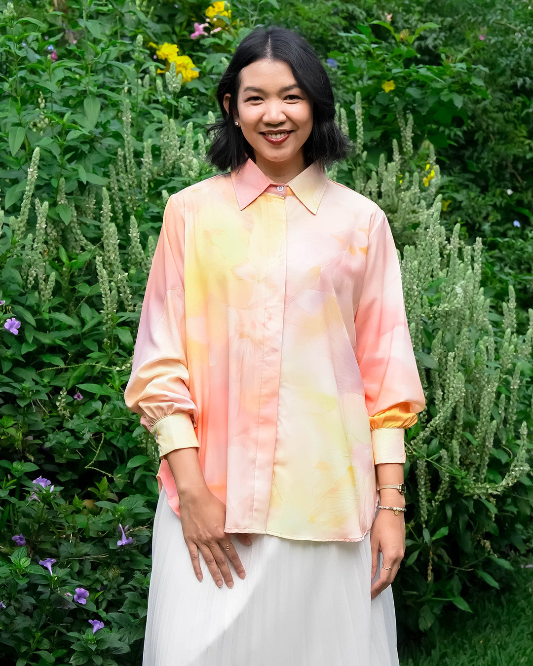 Woman wearing a tie-dye shirt by Puru Kambera standing in a garden