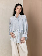 Woman wearing a light blue shirt with lace details by Studio Tui against a beige background