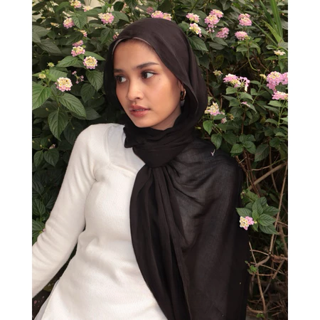 A woman wearing a black pashmina scarf, likely a pashmina, with a garden background.