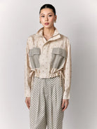 Woman wearing a beige patterned outer by Studio Tui and pants on a light gray background