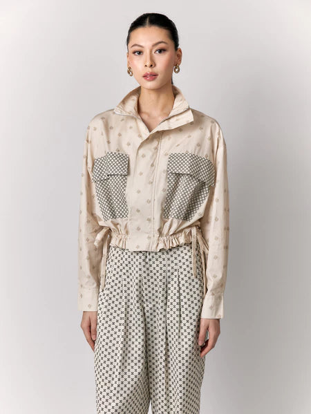 Woman wearing a beige patterned outer by Studio Tui and pants on a light gray background