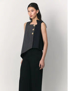 A woman modeling a sleeveless navy black top by Studio Tui with a vertically striped front panel and three gold-tone decorative buttons, paired with black wide-leg pants, against a plain light gray studio background.