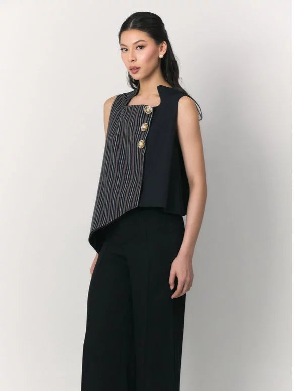 A woman modeling a sleeveless navy black top by Studio Tui with a vertically striped front panel and three gold-tone decorative buttons, paired with black wide-leg pants, against a plain light gray studio background.