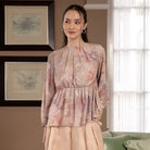 Woman wearing a peach-colored floral blouse by Hijabchic standing in a room with framed artwork on the wall.